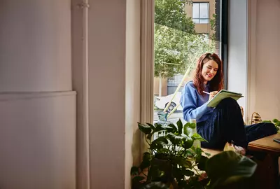 eine Frau sitzt mit einem Tablet und Touchpen auf einer Fensterbank