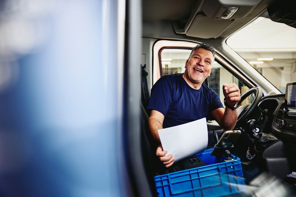 Lächelnder Mann auf dem Fahrersitz eines Logistik-LKWs, der ein Stück Papier hält