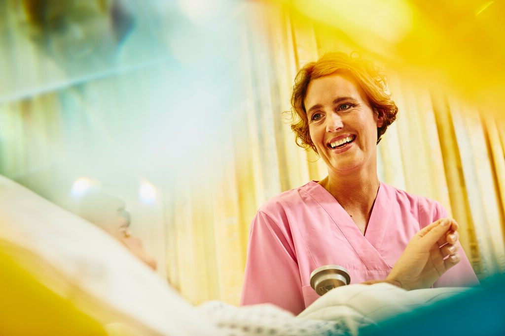 Eine Krankenschwester in rosa Uniform besucht lächelnd einen Patienten.