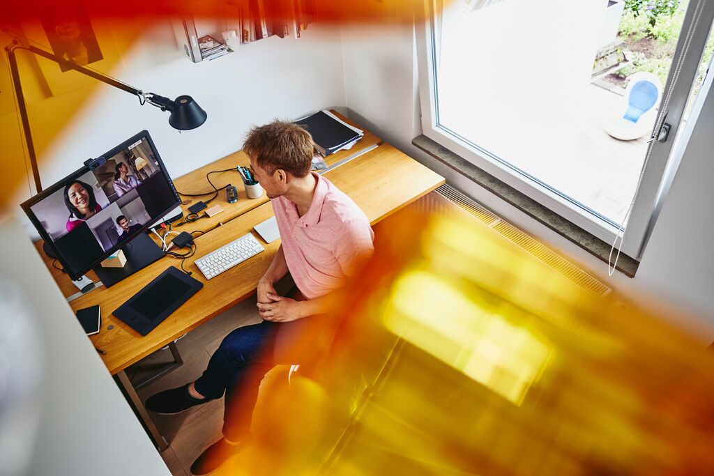Ein Mann sitzt im Homeoffice an seinem PC und spricht mit Kollegen