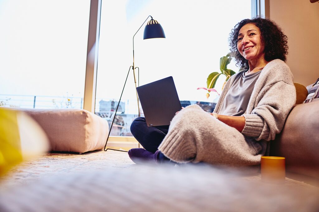 Lächelnde Frau im Schneidersitz mit Laptop