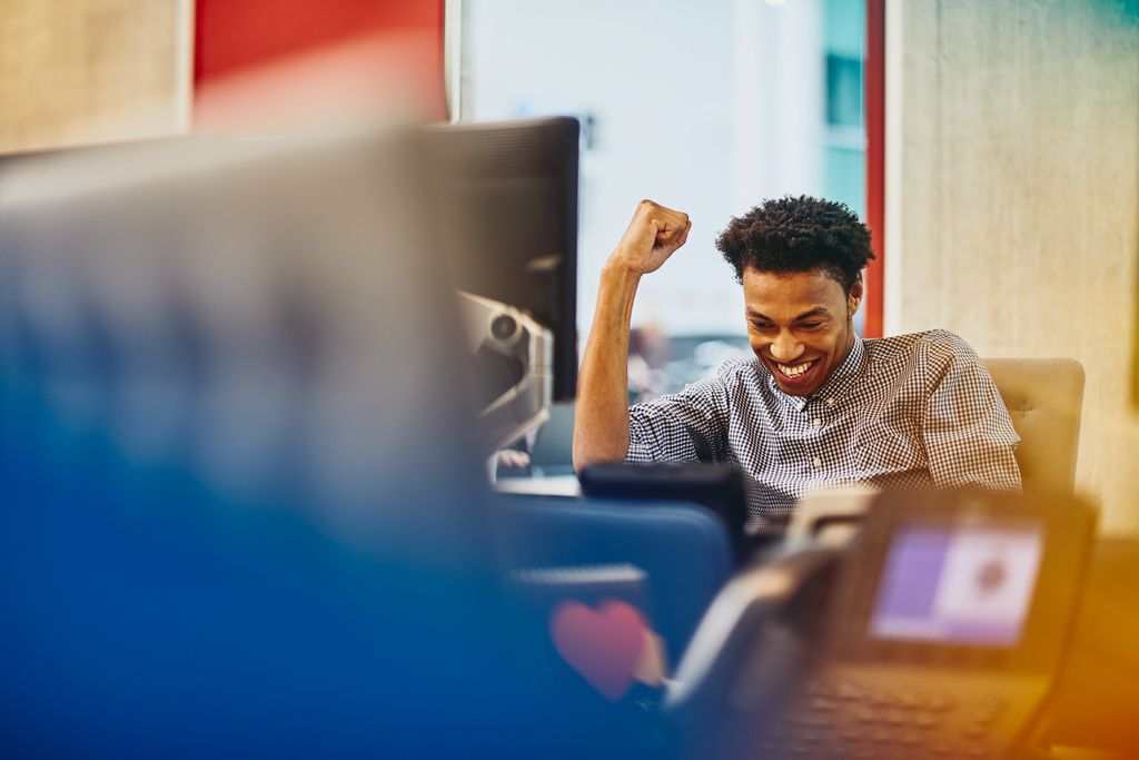 Mann sitzt an einem Schreibtisch in einem Büro und lächelt glücklich.