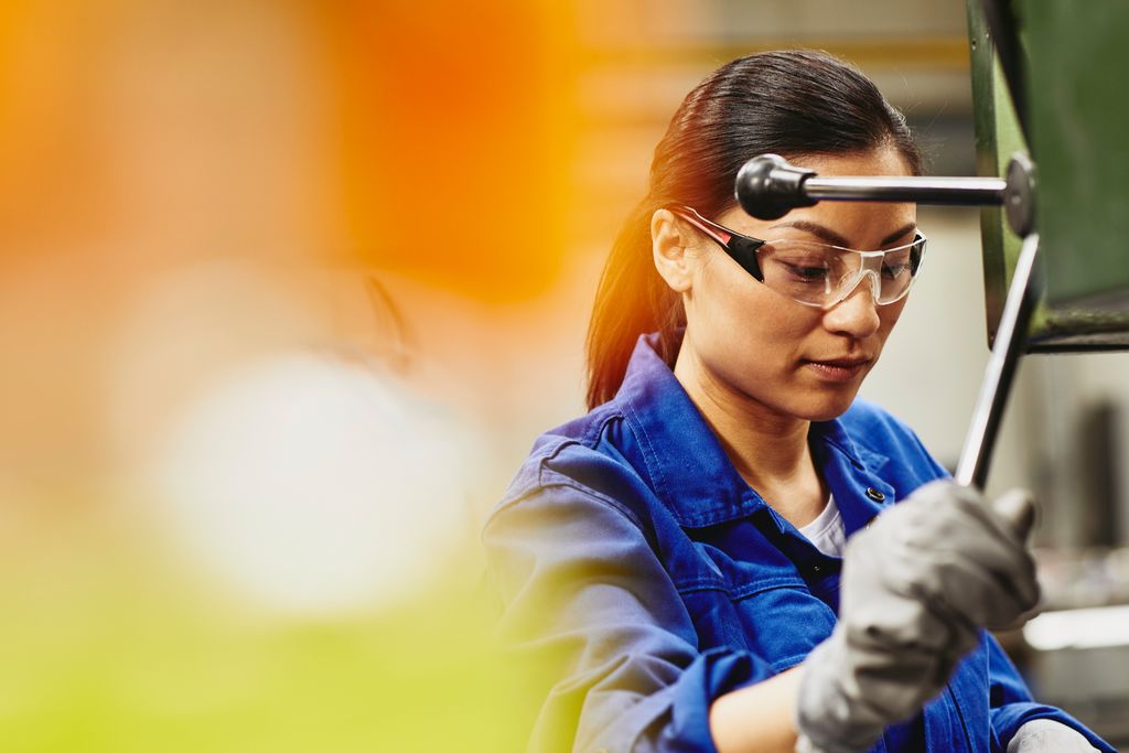 Gewerbliche Mitarbeiterin mit Schutzbrille und Handschuhen an einer Maschine arbeitend
