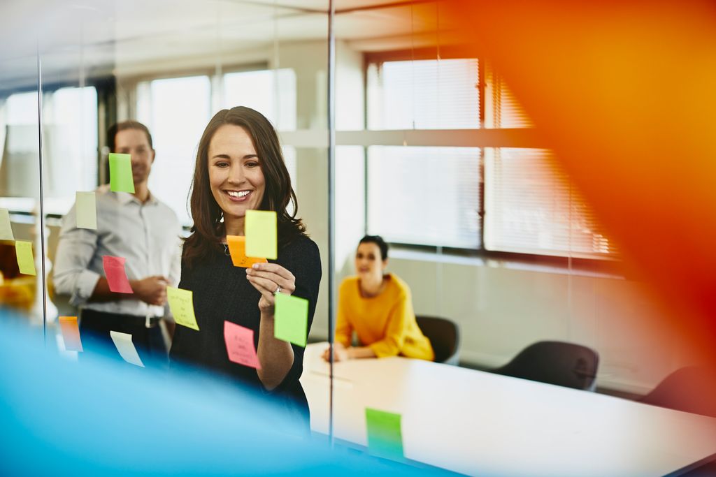 Zwei Geschäftsfrauen und ein Mann in einem Büro kleben Klebezettel an ein Fenster.