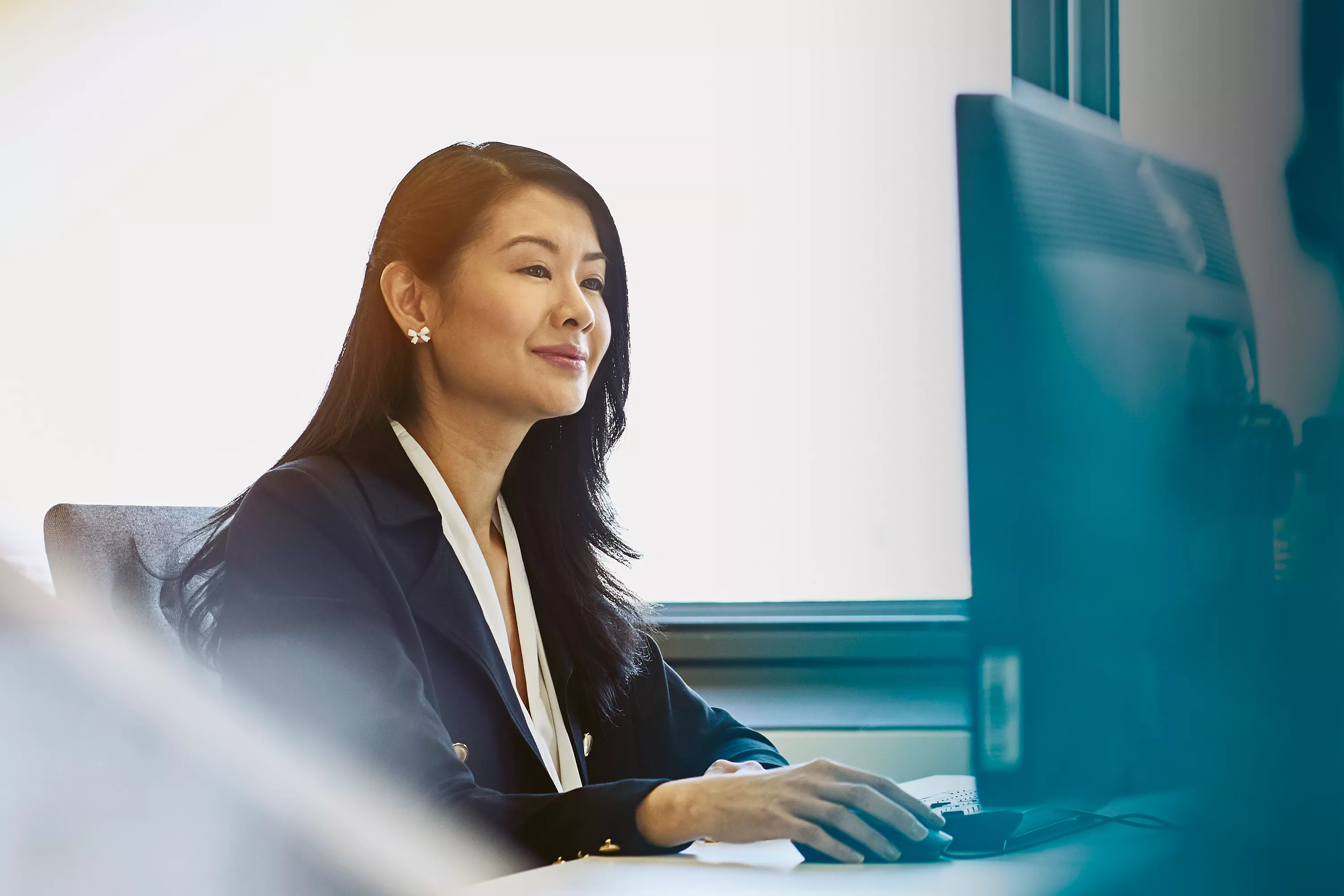 Portrait einer Frau, die an einem Arbeitsplatz sitzt und auf ihren Monitor blickt