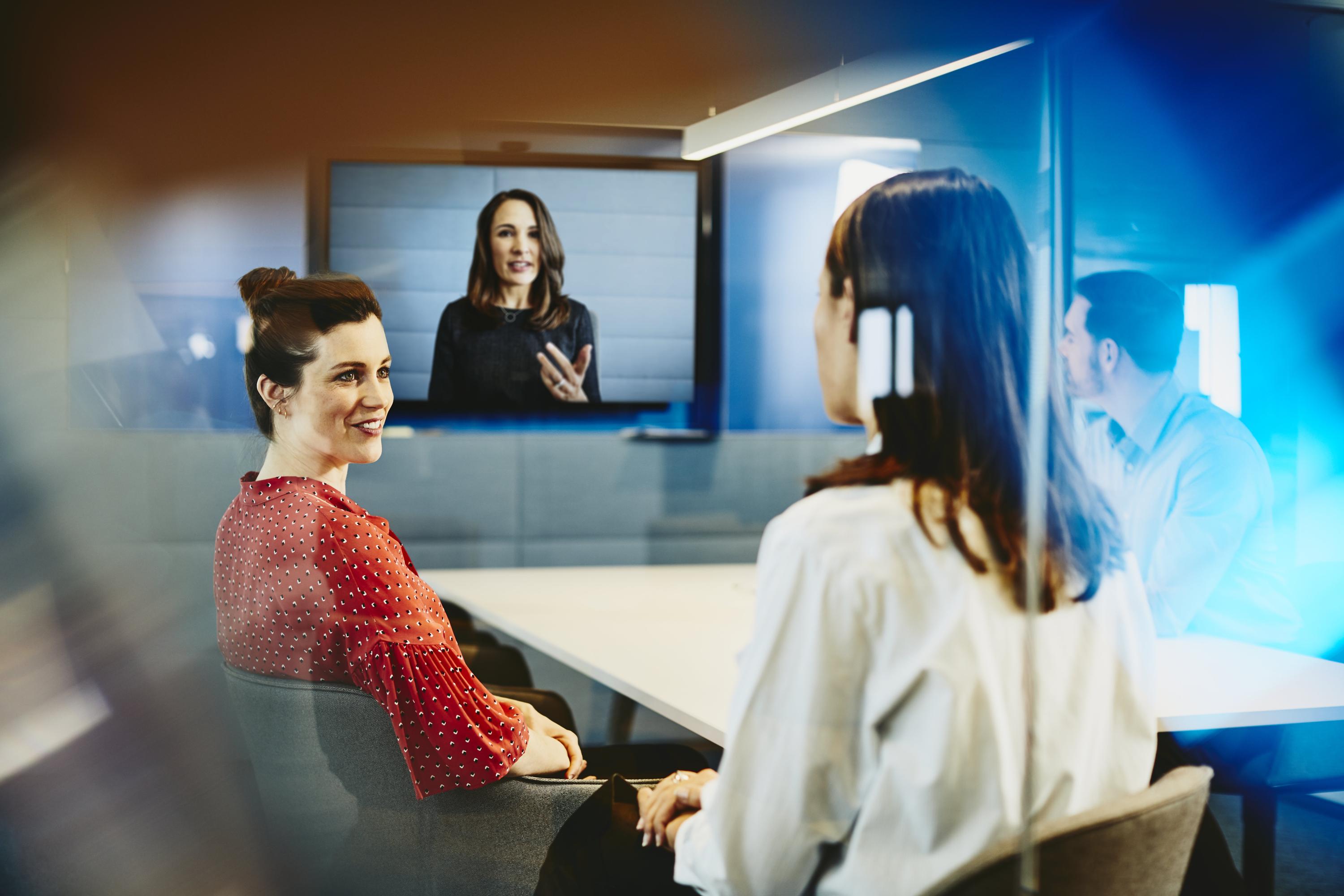 Two business women and a man in an office having a Hangout. Primary color: blue.