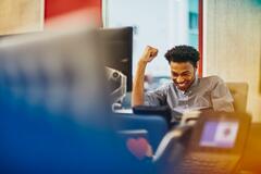 Mann sitzt an einem Schreibtisch in einem Büro und lächelt glücklich.