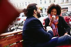Ein Mann und eine Frau sitzen mit Kaffeebechern auf einer Bank und unterhalten sich