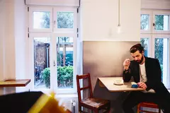 ein Mann sitzt an einem Hochtisch in einem Bistro und blickt auf sein Smartphone