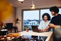 ein Mann und eine Frau stehen in der Wohnküche und blicken auf ein Laptop