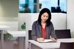 Frau sitzt an einem Tisch und schreib in ein Buch