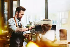 Mann mit tätowiertem Arm schäumt Milch an einer Kaffeemaschine auf
