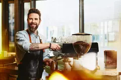 Mann mit tätowiertem Arm, der Kaffee zubereitet