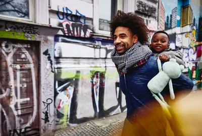 ein Mann trägt Kleinkind auf dem Rücken durch die Stadt