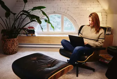 eine Frau sitzt in einem Sessel und blickt auf ein Laptop