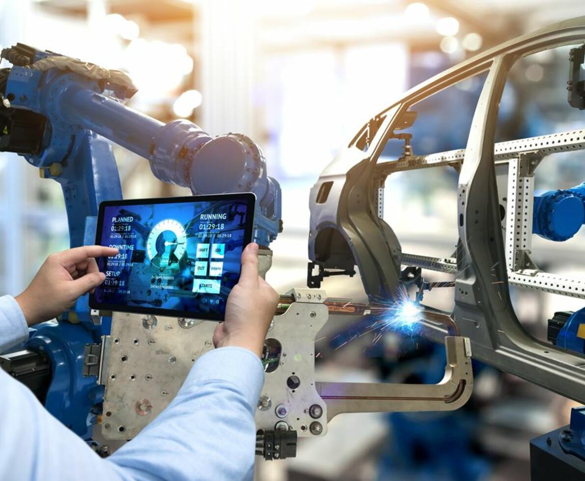 Mann steuert per Tablet einen Schweißroboter an einer Autokarosserie