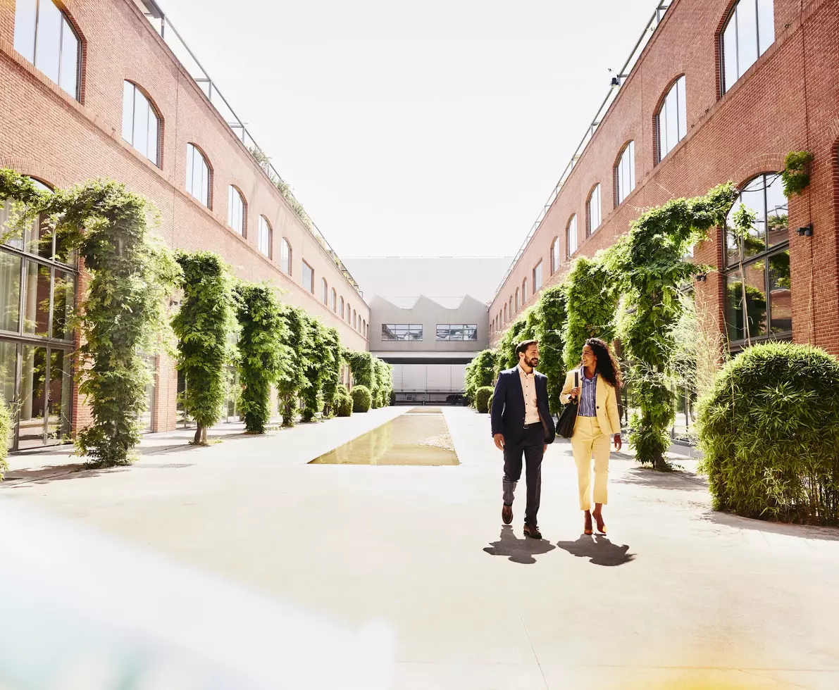 ein Mann und eine Frau in Business-Kleidung laufen über einen Innenhof