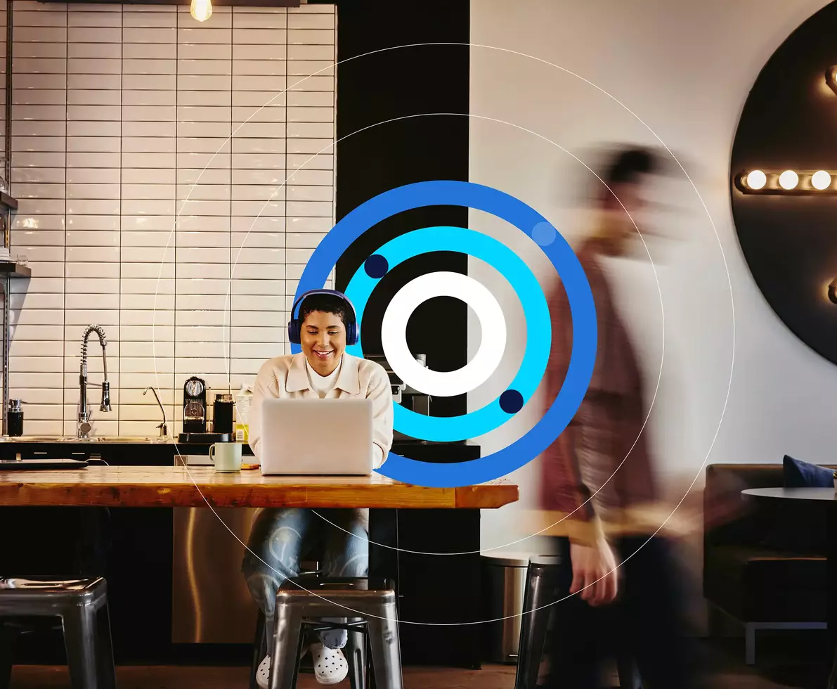 eine Person arbeitet mit Kopfhörern am Laptop in einem Café, während ein Mann vorbeigeht