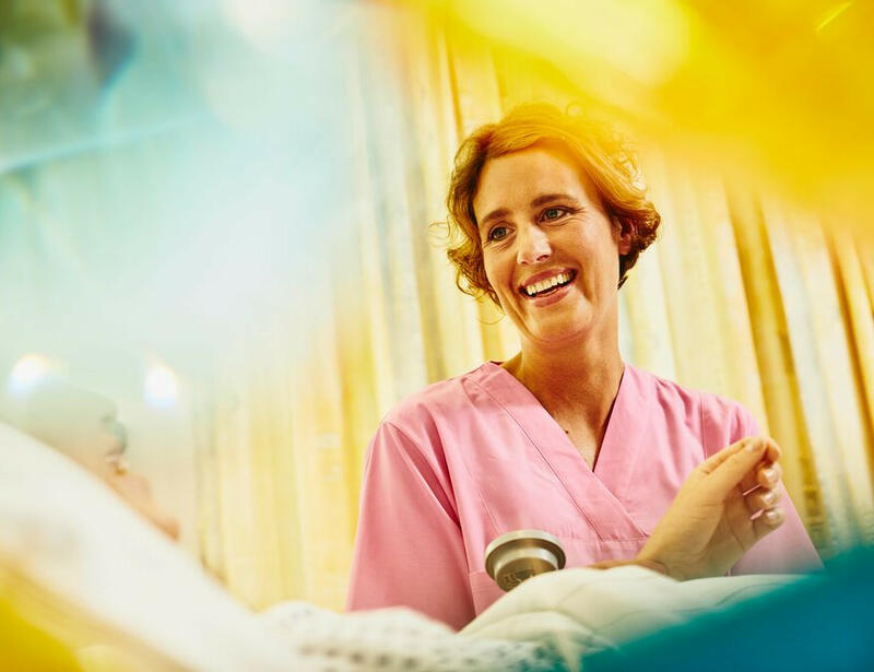 Eine Krankenschwester in rosa Uniform besucht lächelnd einen Patienten.