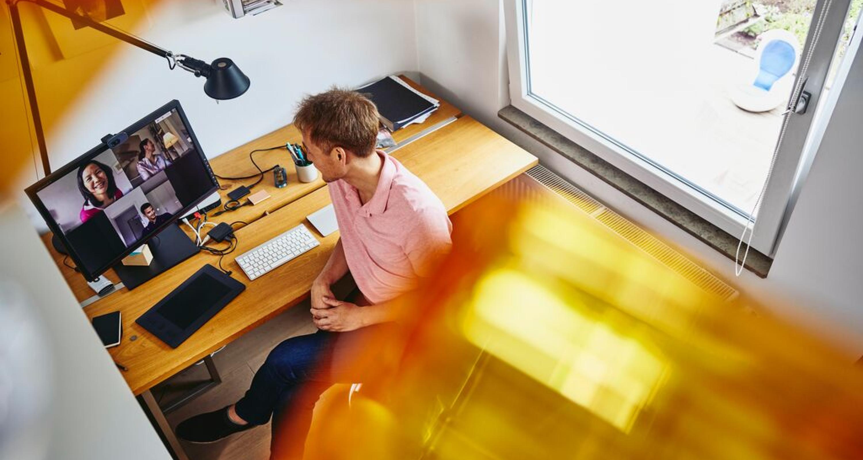 Ein Mann sitzt im Homeoffice an seinem PC und spricht mit Kollegen