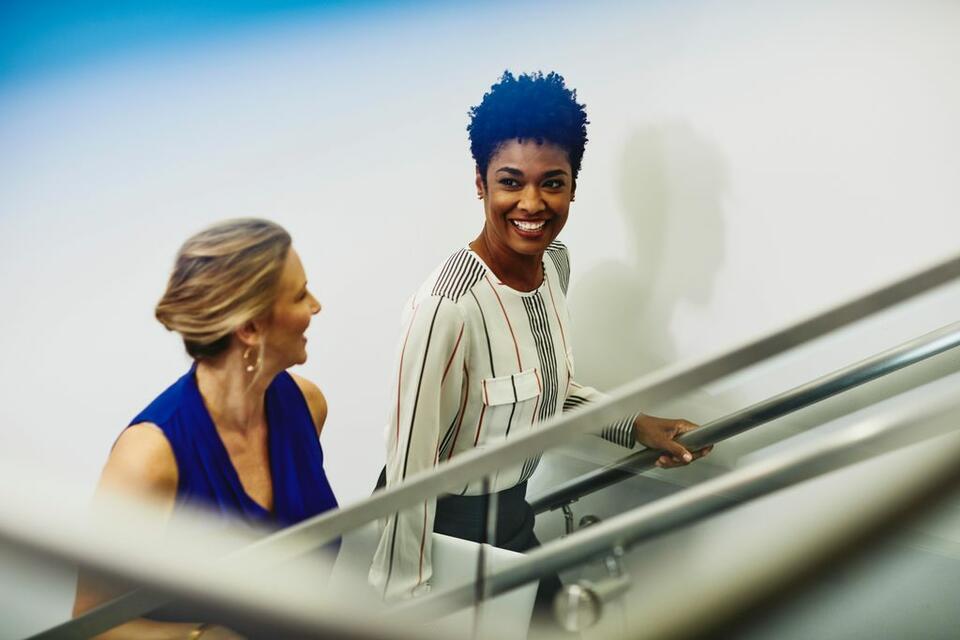 Zwei lächelnde Frauen gehen die Treppe hinauf.