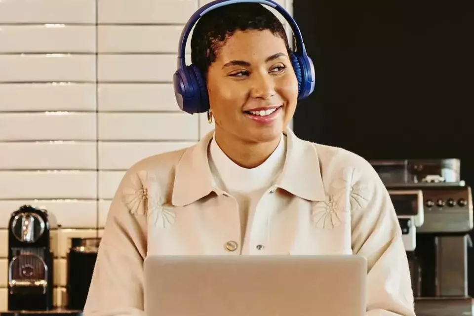 Frau mit Kopfhörern sitzt vor ihrem Laptop und blickt lächelnd zur Seite