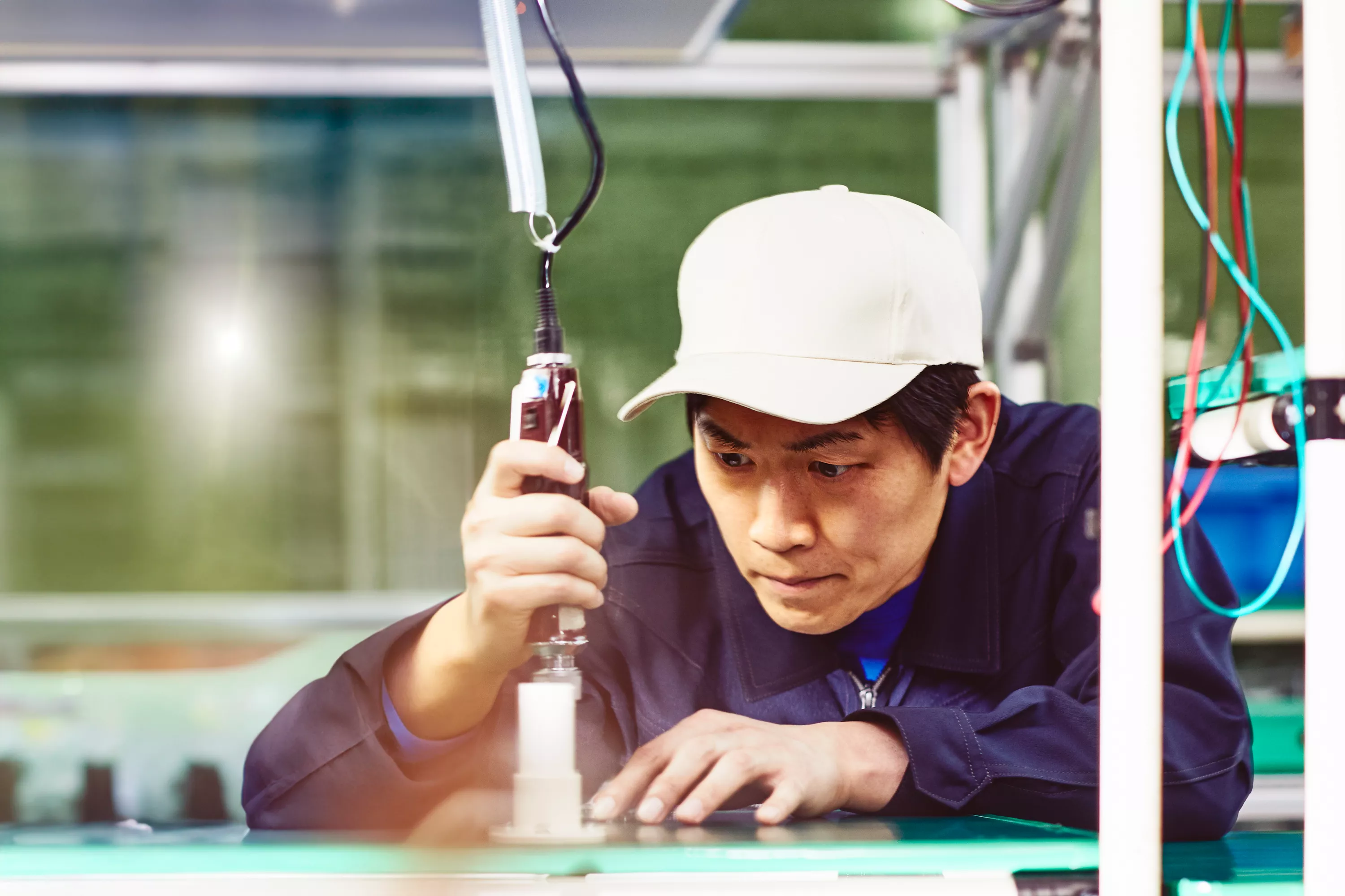 Mann mit weißer Kappe und blauem Overall, der mit Werkzeugen auf einer Produktionsstätte arbeitet