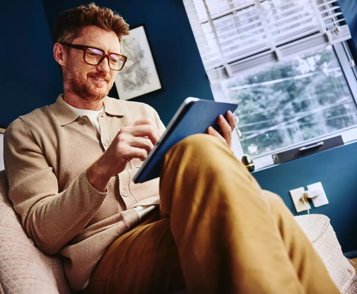 ein Mann sitzt auf einem Sessel und schaut auf ein Tablet