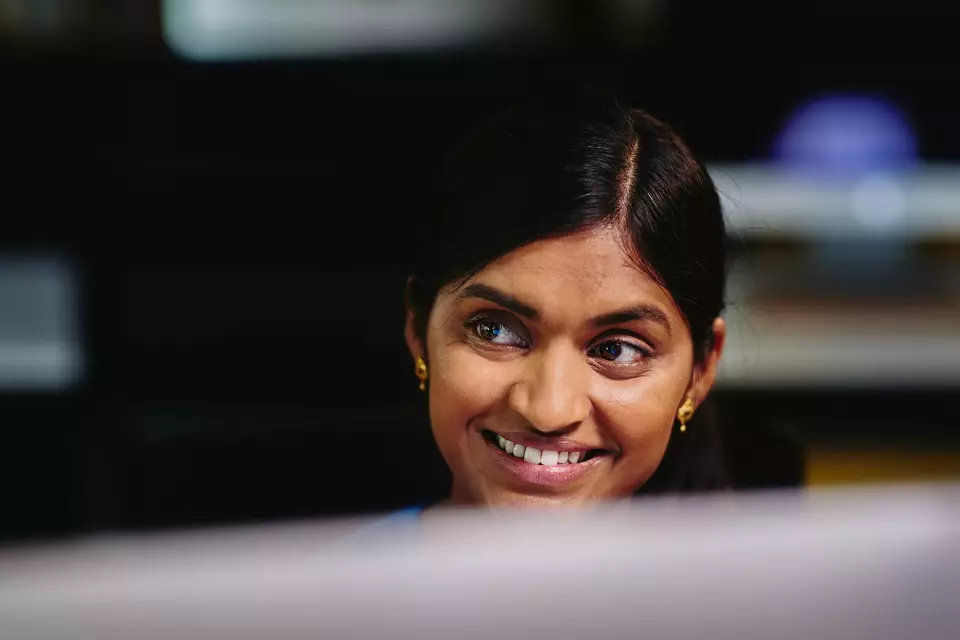 Frau sitzt lächelnd vor einem Bildschirm und blickt zur Seite